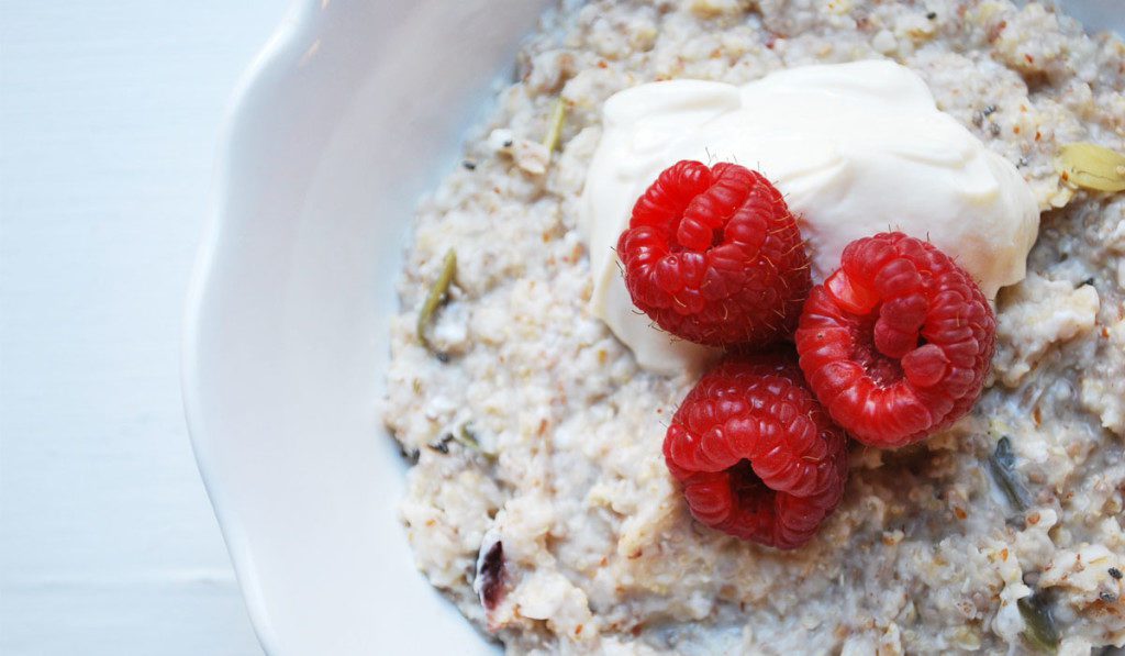 A bowl of oatmeal with raspberries and cream on top